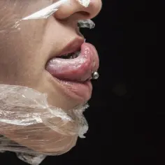 Język z kolczykiem, owinięty folią. Ten piercing języka, zwany venom piercing, dodaje odważnego charakteru.