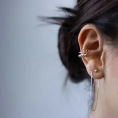 Ucho z kilkoma kolczykami, w tym ozdobnym forward helix piercing z koralikami i długim łańcuszkiem.