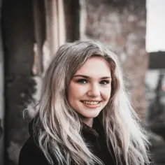 Uśmiechnięta dziewczyna z blond włosami i kolczykiem w wardze, jej skóra wygląda na gładką i zdrową.