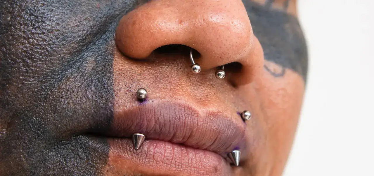 Osoba z tatuażem na twarzy i licznymi kolczykami, w tym angel bites piercing.