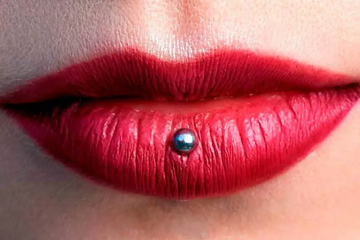 Usta z czerwoną szminką i błyszczącym, srebrnym kolczykiem typu ashley piercing.